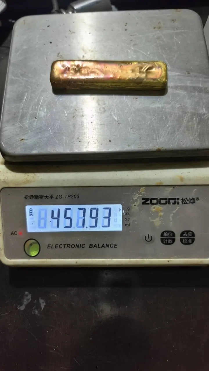A poured gold doré bar resting on an electronic balance reading 458.93 grams