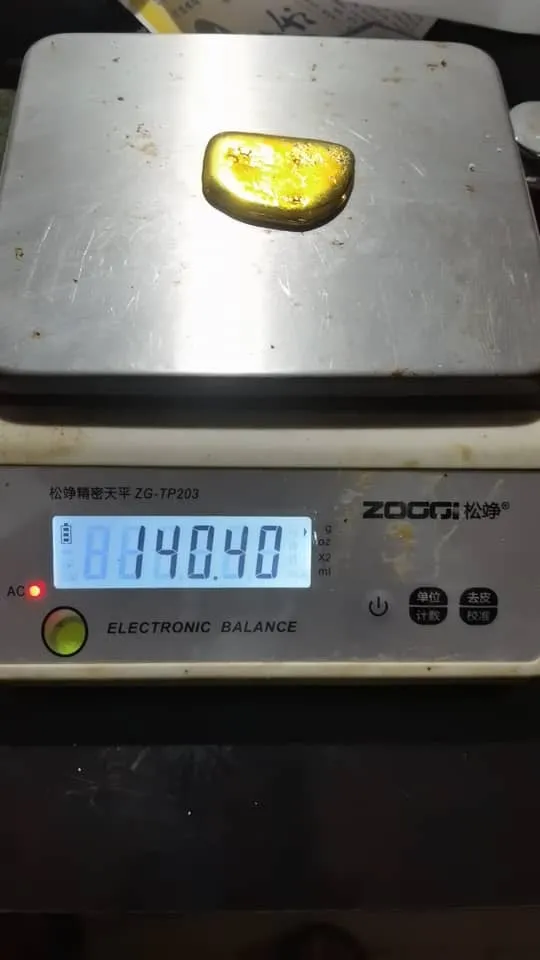 A smooth gold doré button on an electronic balance reading 140.40 grams