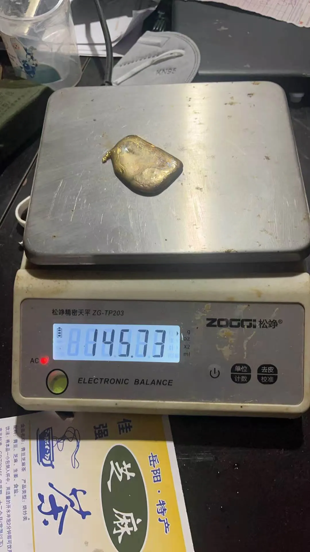 A rounded gold doré button on an electronic balance reading 146.73 grams