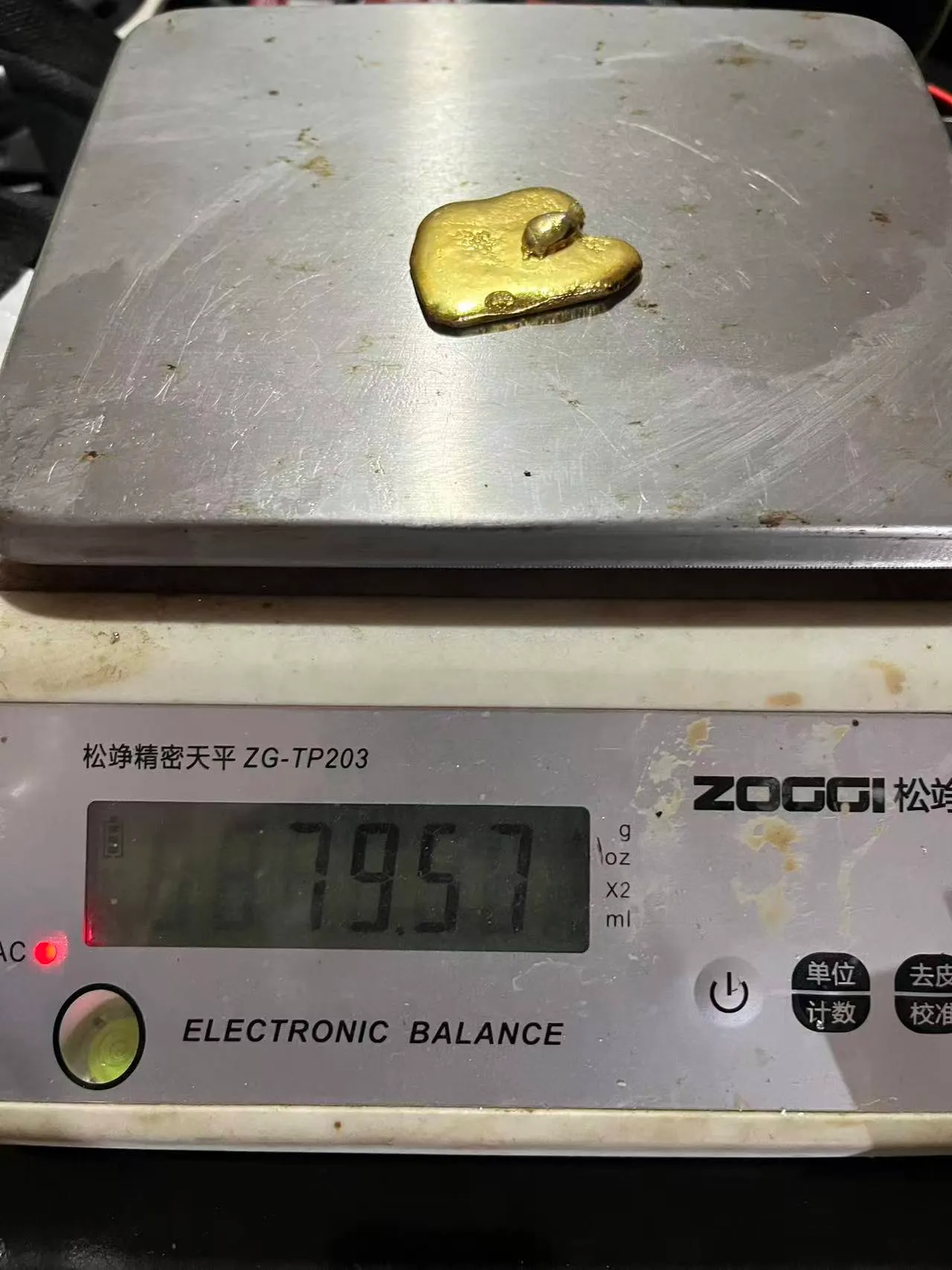 A small gold doré button on an electronic balance reading 79.57 grams