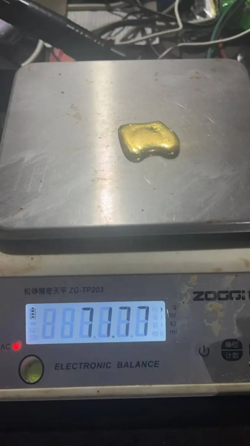 A poured gold doré button being weighed on an electronic balance
