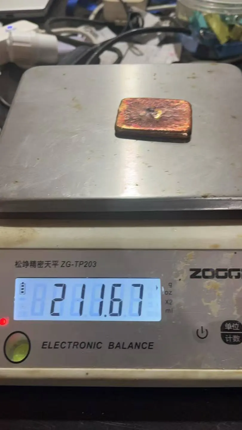 A rectangular cast gold ingot on an electronic balance reading 211.67 grams